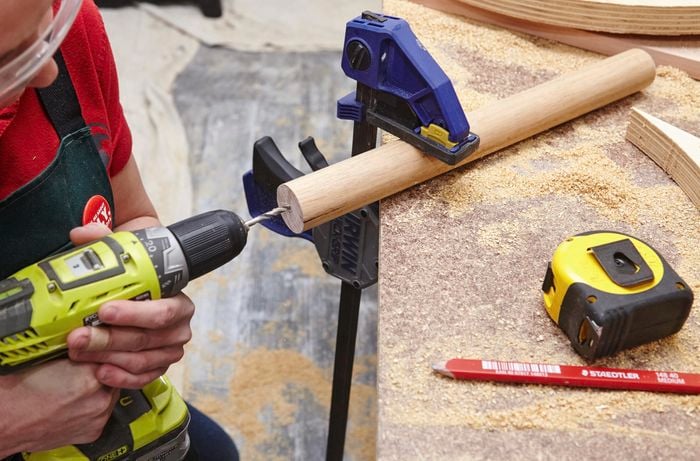 A person drilling a hole in a piece of dowel using a cordless drill