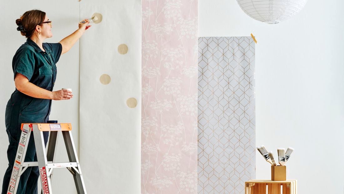 Woman painting circles on a paper strip on a wall.