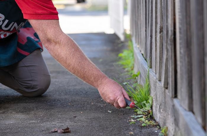 A person removing plants and dirt near the fence.