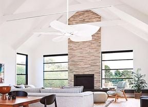 A modern living room featuring a timber dining table, grey lounge, cream brick fire place and a white ceiling fan.
