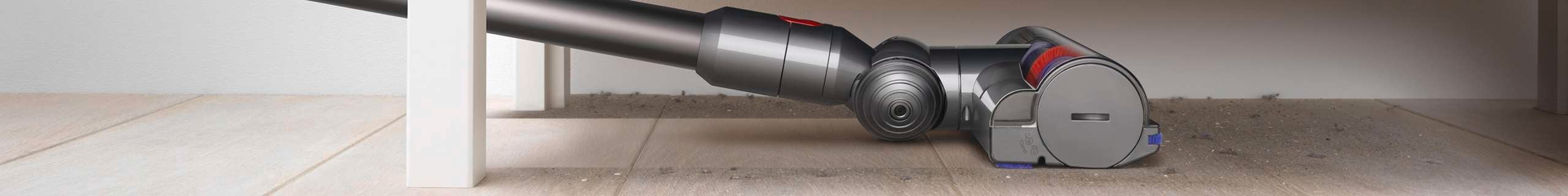 A Dyson vacuum vacuuming floorboards under a dresser drawer.