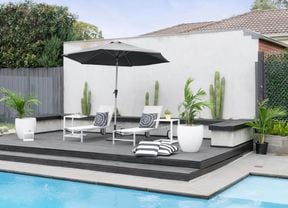 A wide shot of an outdoor pool area, with umbrella, sunbeds and throw cushions