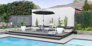 A wide shot of an outdoor pool area, with umbrella, sunbeds and throw cushions