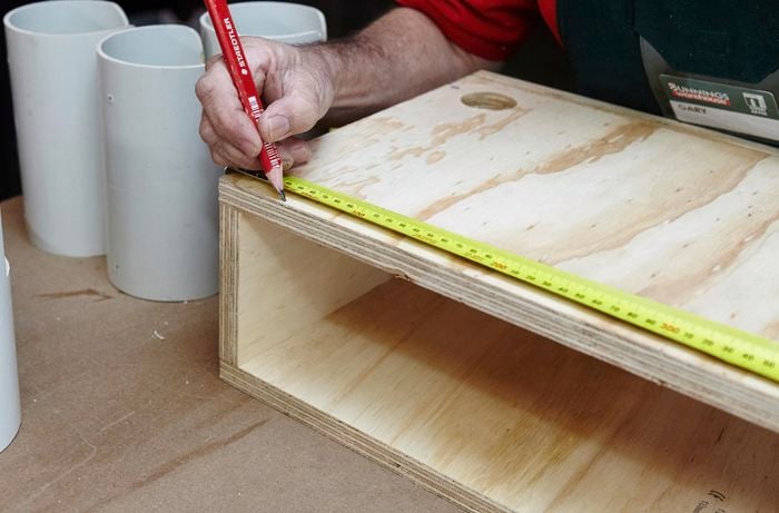 A person marking a measurement on a plywood box