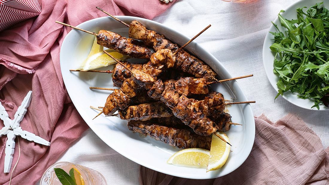  A white platter piled with chipotle chicken skewers with a bowl of rocket leaves on the side