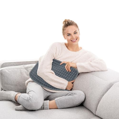 A lady lying on a couch with a heat pack on her belly