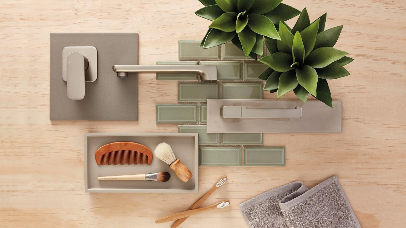 Flatlay image of bathroom fixtures including a stainless steel basin mixer tap and shower mixer tap, green mosaic tiles and grooming items