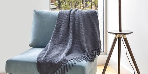 A blue armchair with a throw on it and a lamp.