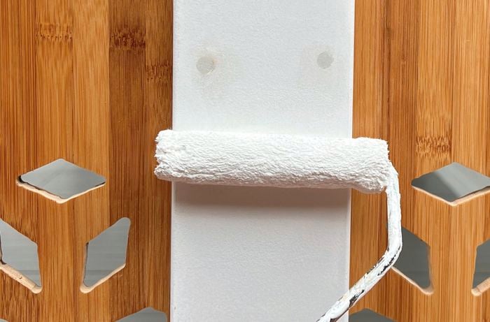 A paint roller with white paint is used to paint the back of the frame.