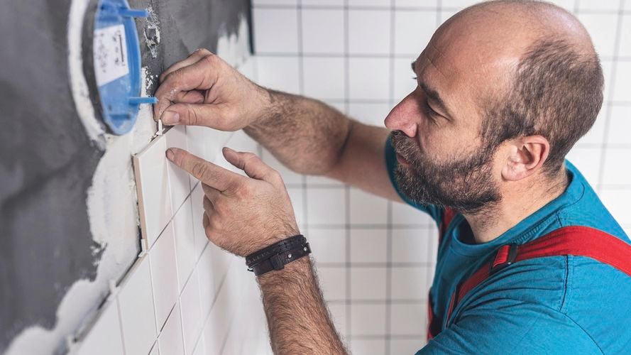 man fixing a tile in a bathroom