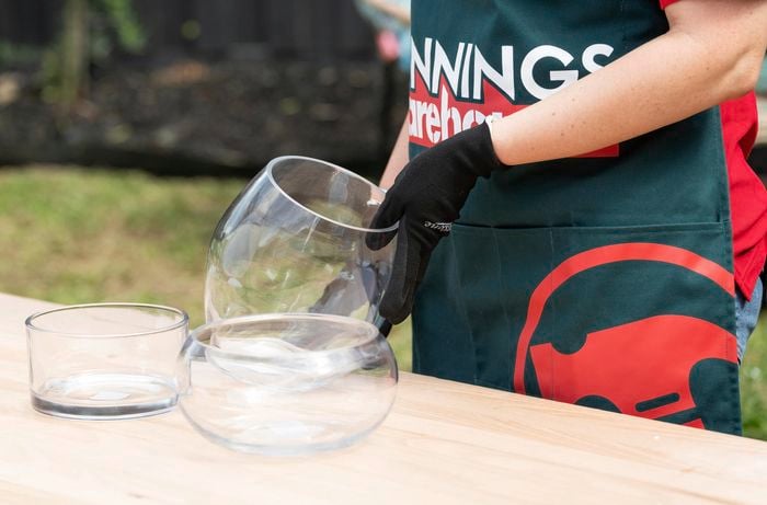 Three see-through glass pots sitting on table outside, with a person holding one of them on an angle.