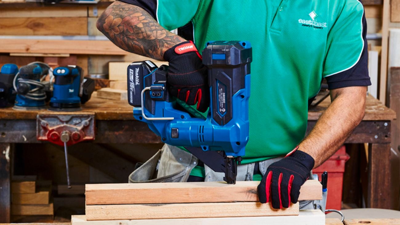  A close up of a tradie in a bright green t-shirt using a Makita framing nailer in a workshop
