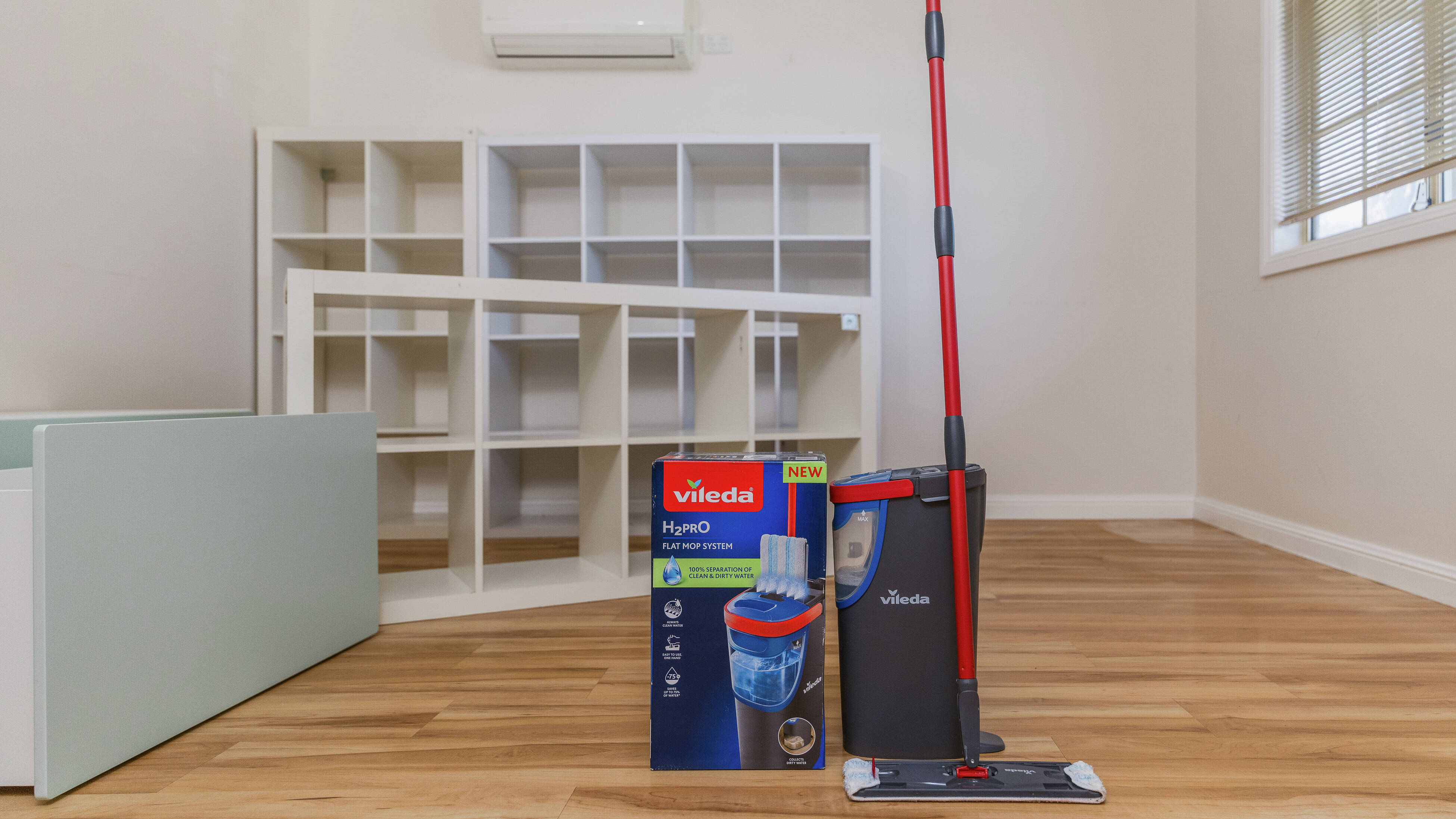 Empty, freshly cleaned room with wooden floors, white shelving, and cleaning equipment including a mop and bucket.