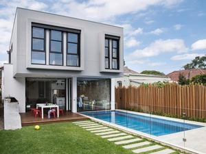 A backyard with a lawn, pavers, pool and deck.