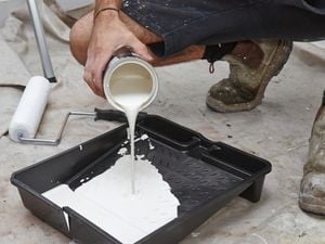 A pot of white paint being poured into a painters tray