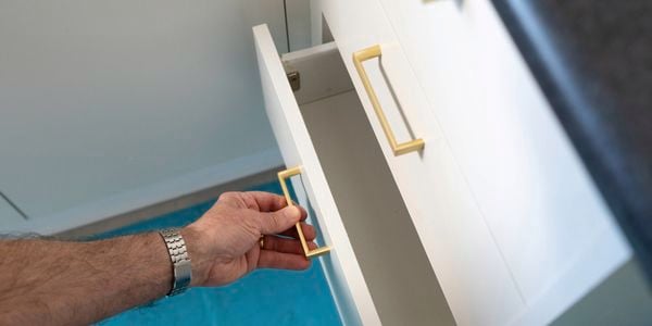 A person is opening a freshly painted white drawer with a gold handle in the kitchen.