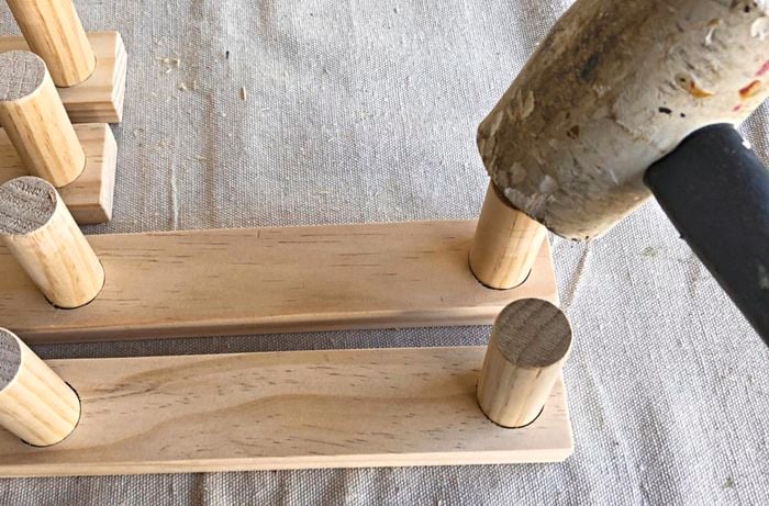 A mallet being used to knock a length of dowel into a hole in a pine board