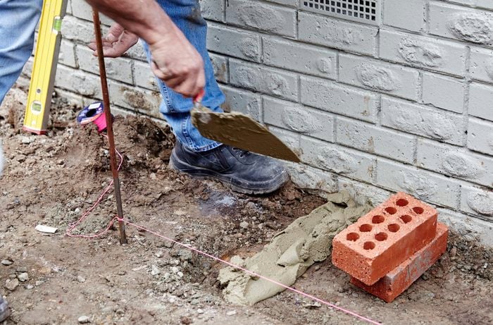 A person laying a line of mortar on the ground at right angles to a house wall