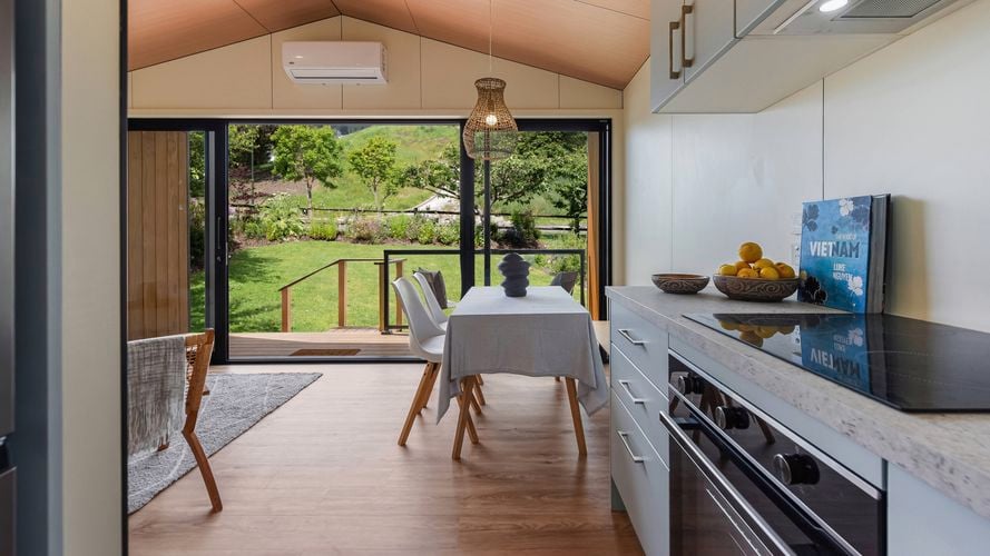 Open-plan living and dining area with kitchen, high ceiling and deck outlook.