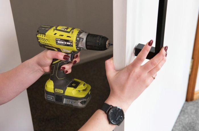 A person attaching a door handle to a wardrobe door using a cordless drill