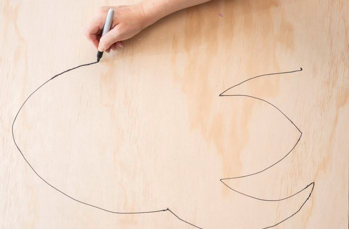  A person is sketching a rocket shape outline on a plywood board as part of a DIY clock upcycle project.