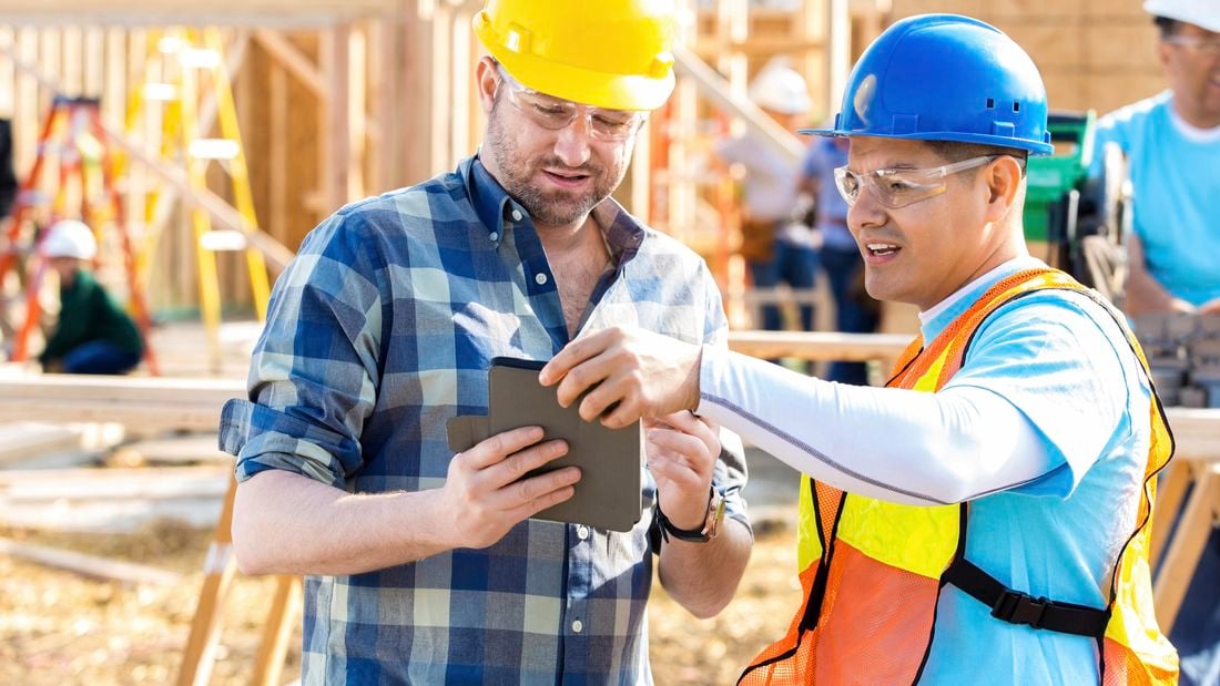 Two construction workers looking at a tablet device while on a construction site