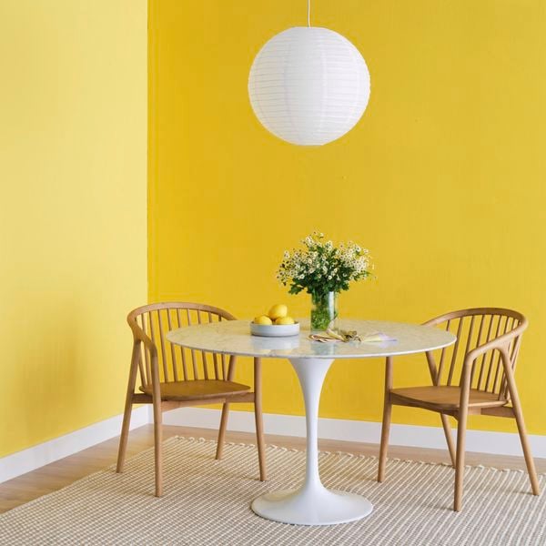 White marble dining table with tulip base on a neutral rug with two timber dining chairs beneath a round paper lantern pendant light