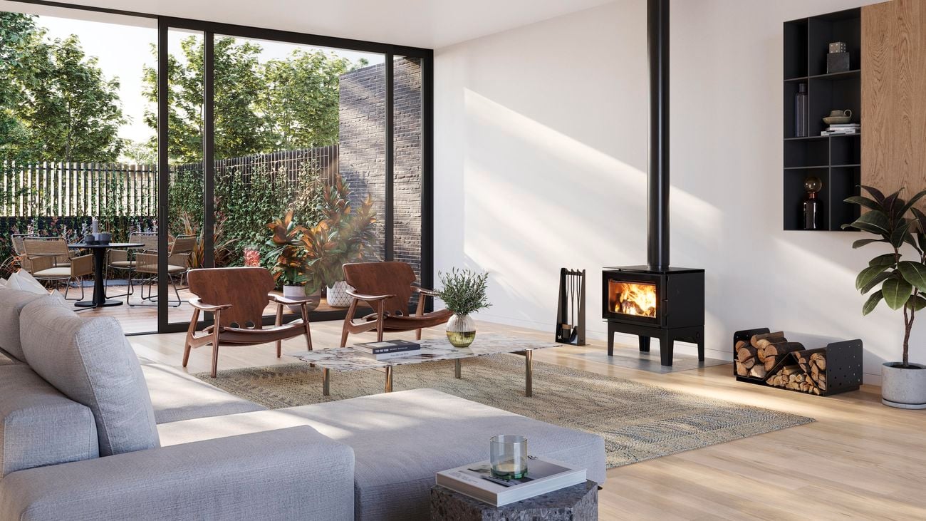 A Masport ‘Bowden Legs’ indoor wood heater in a cosy living room featuring timber armchairs and a grey chaise sofa