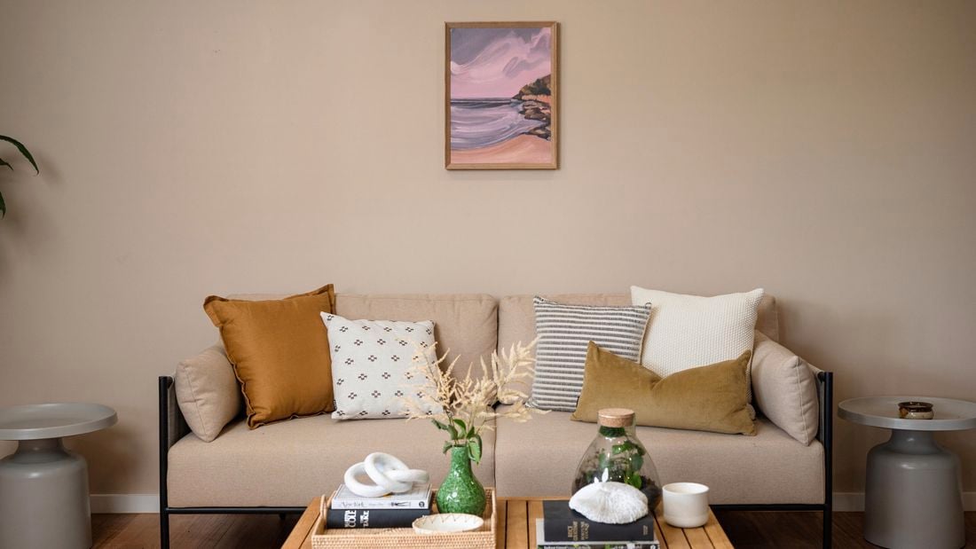 Lounge room with a couch with cushions on it, a picture hanging on the wall and a coffee table in it