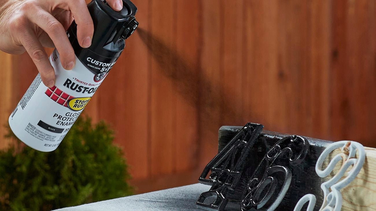 Hand sprays black spray out of can over white numbers
