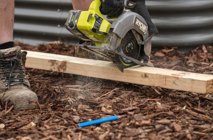 A person holding a power tool against a piece of timber