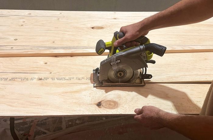 A close up of a hand using a circular saw to cut timber