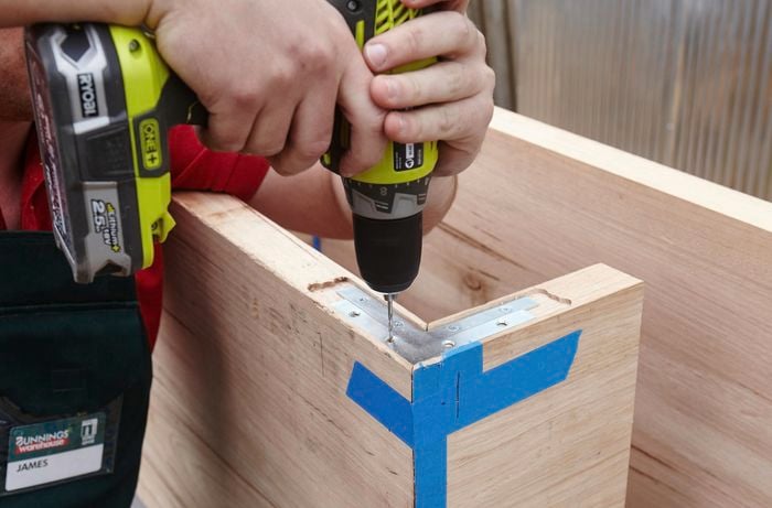 A person screwing an L bracket into a two pieces of timber joined at right angles