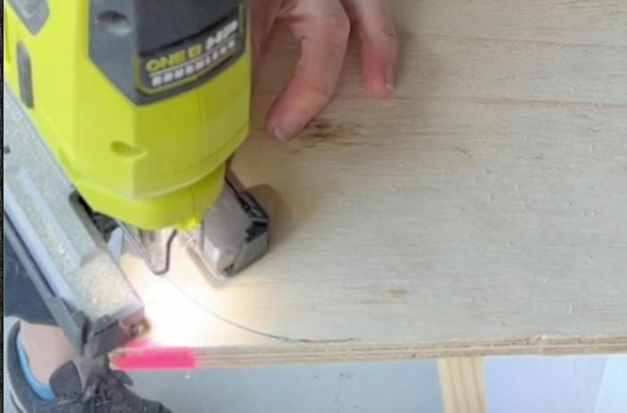 Jigsaw cutting through piece of plywood to form curves on back panel of bedhead.