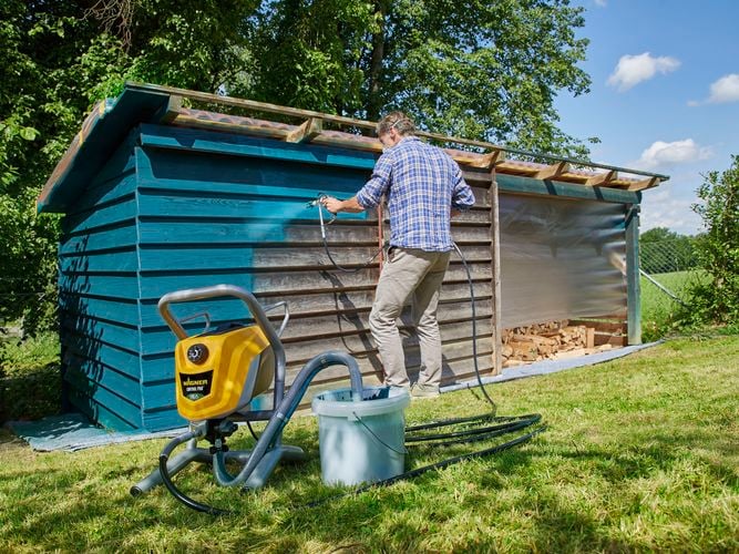 Wagner Control Pro 250M spraying teal paint to a wooden shed to rejuvenate it.