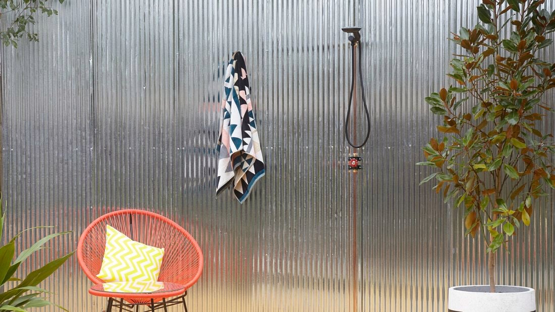 Outdoor shower area with orange wire chair and towel hanging off hook.