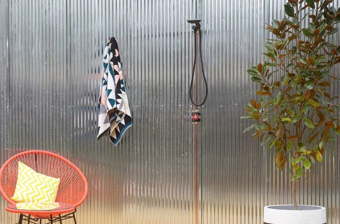 Outdoor shower area with orange wire chair and towel hanging off hook.