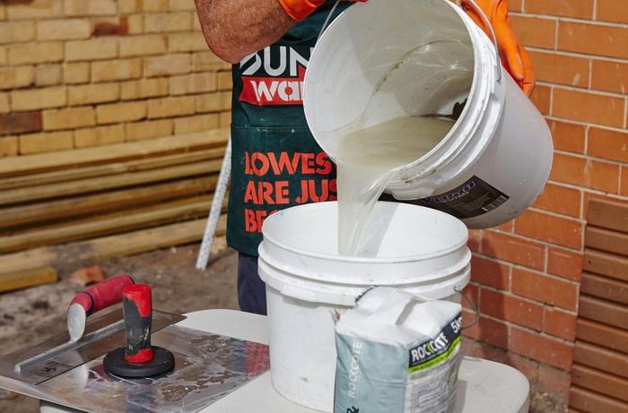 A person pouring water into a mixing bucket