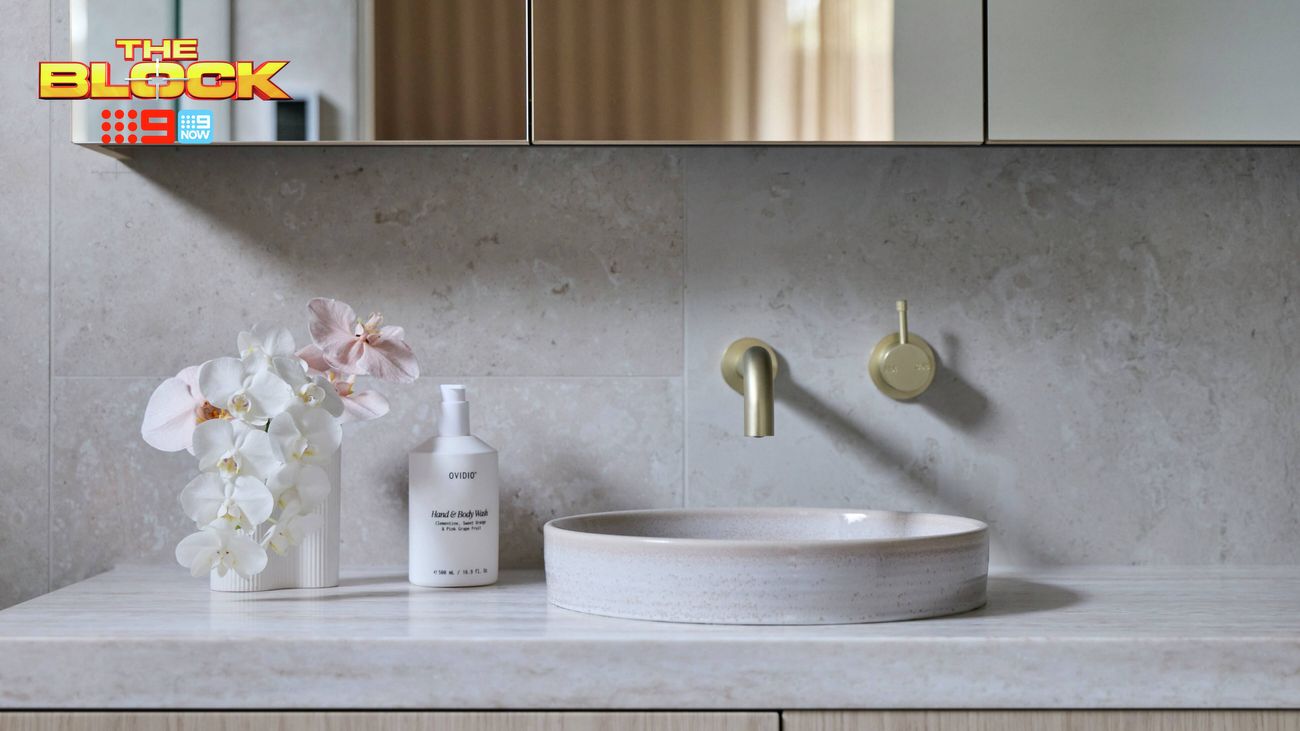 Close-up of a bathroom vanity featuring a round basin, brushed brass wall-mounted tapware and light timber cabinetry.
