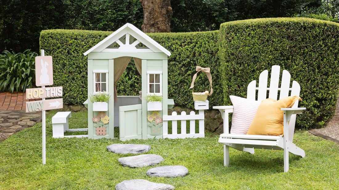 Backyard setting with Easter craft projects including egg hunt sign and painted cubby house