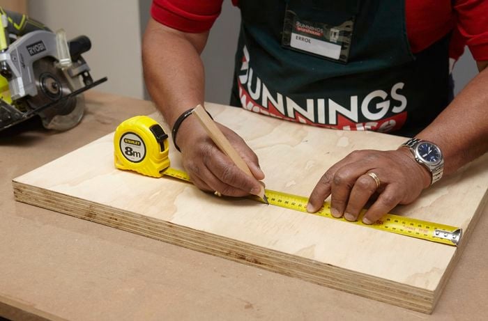 Person using measuring tape and pencil to mark up piece of ply wood.