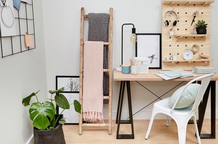 Home office with desk, chair, plant, timber ladder, and pegboard shelf.