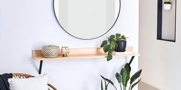 A round mirror, timber shelf, chair styled with throw and cushion and indoor plants in pots.
