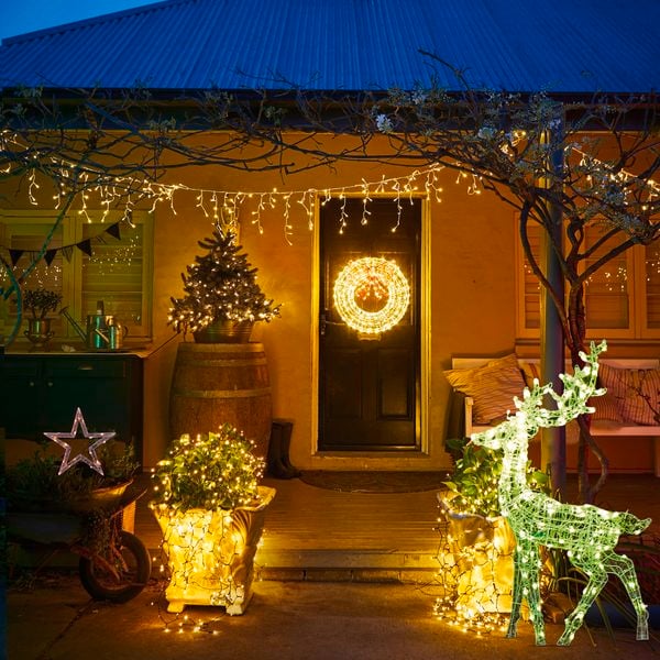 Fairly lights and an illuminated reindeer decorate the front of an old style house at night