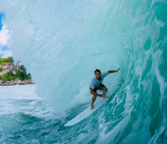 Surfer riding inside the barrel of a large turquoise wave on a white surfboard.