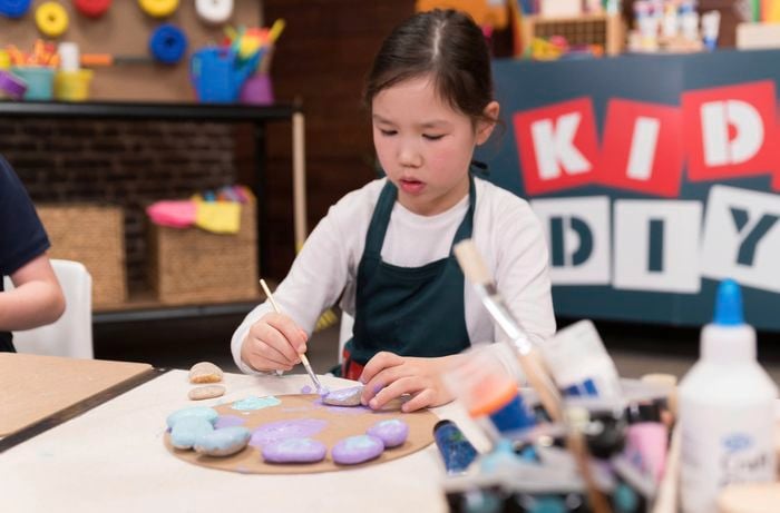 A girl is colouring the pebbles purple and blue for the tic tac toe game.