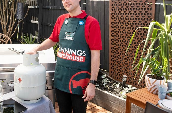 A person standing beside a gas bottle next to a BBQ