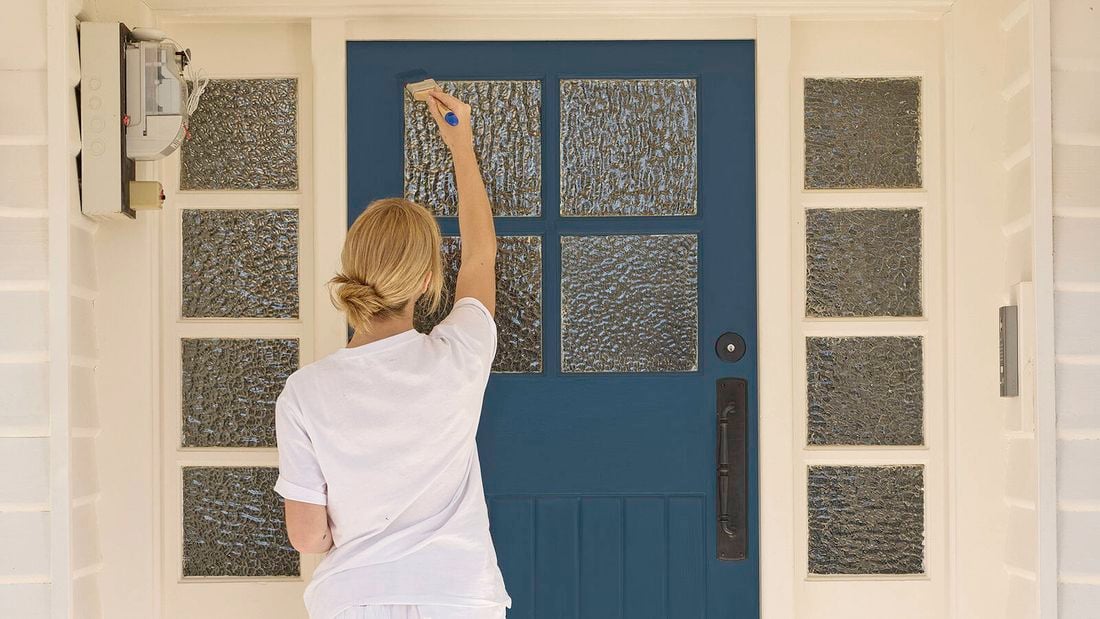 A woman in a white t-shirt painting a blue front door.