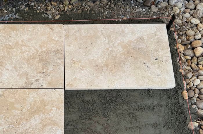 Square beige pavers set into fresh dark mortar, with loose gravel around the border.