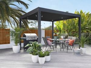 Gazibo with outdoor chairs, table, plants, barbeque and lights.